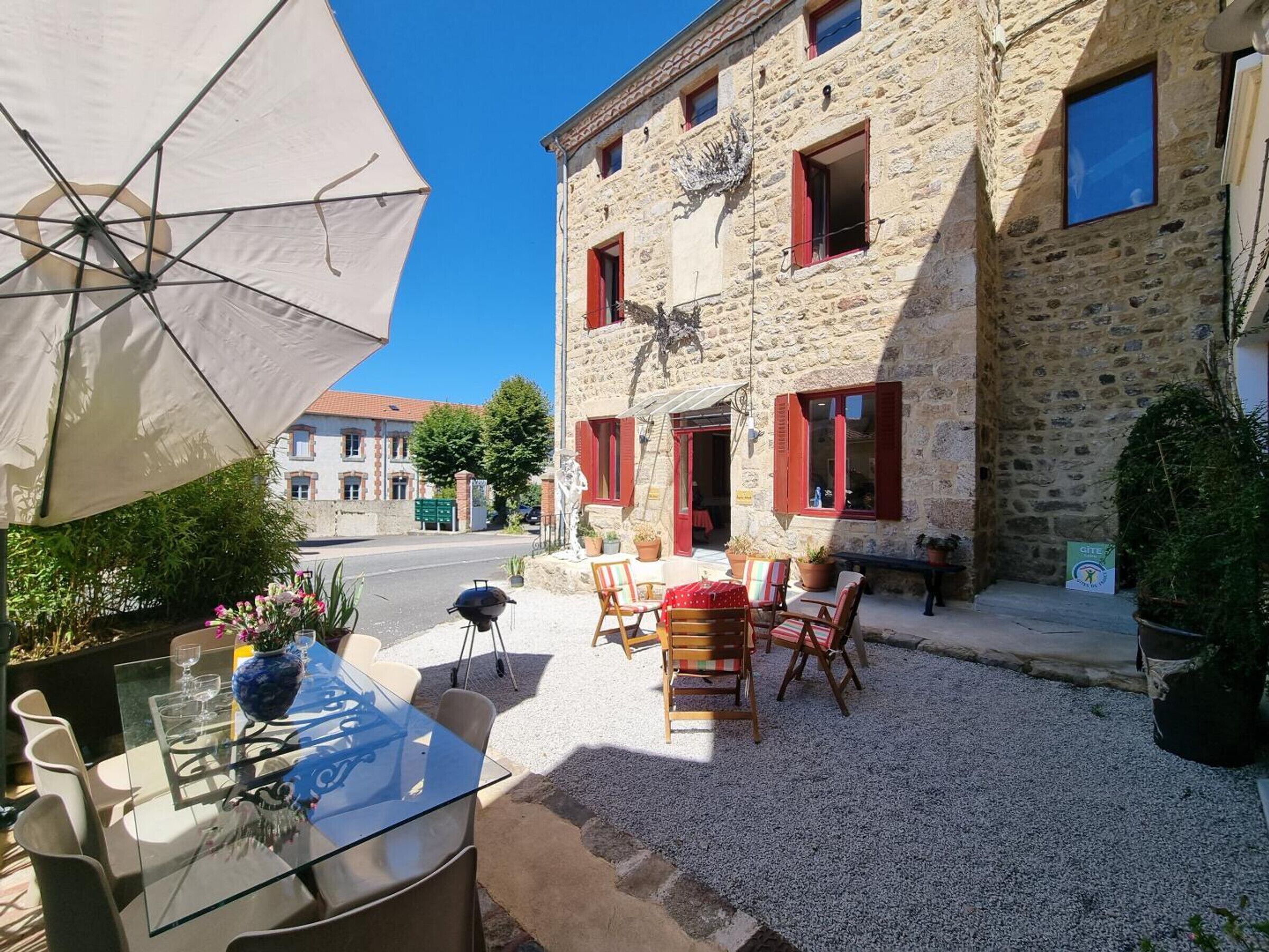Un'area esterna con posti a sedere, un tavolo, sedie, un barbecue e un edificio in pietra con persiane rosse.
