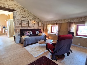 A cozy living room with a stone wall, a sofa, a small round table, and a window with curtains. - Authentic house in the village center - 6 guests (ROZIER COTES D'AUREC)