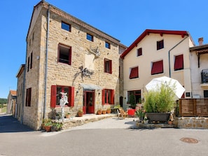 A stone building with red shutters, a white umbrella, and potted plants. - Authentic house in the village center - 6 guests (ROZIER COTES D'AUREC)