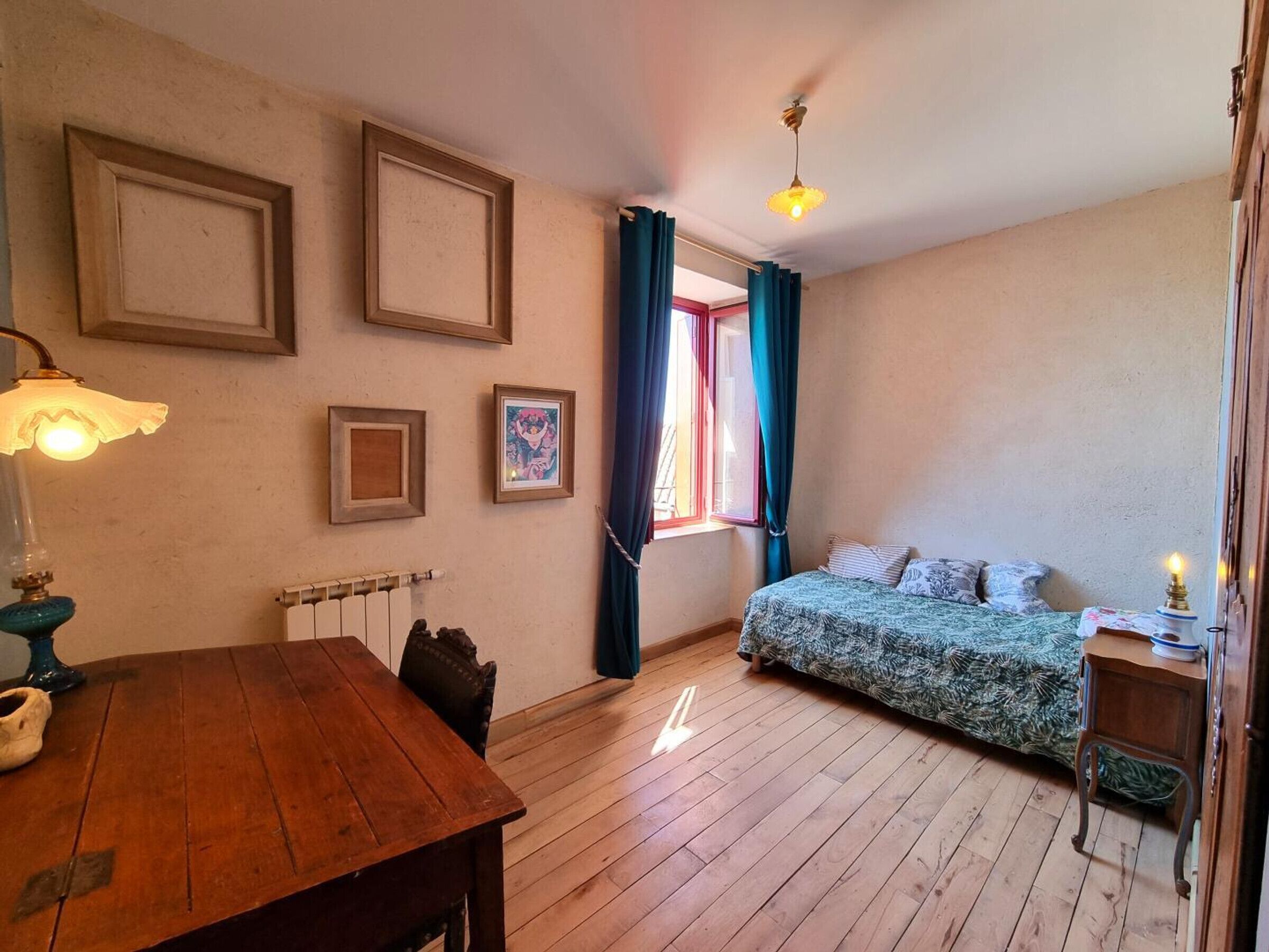 Una habitación con piso de madera, una cama con ropa de cama estampada, una mesa con lámpara y un radiador.