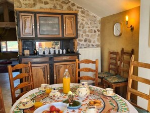A dining area with a table set for breakfast, wooden chairs, a stone wall, and a clock on the wall. - Authentic house in the village center - 6 guests (ROZIER COTES D'AUREC)