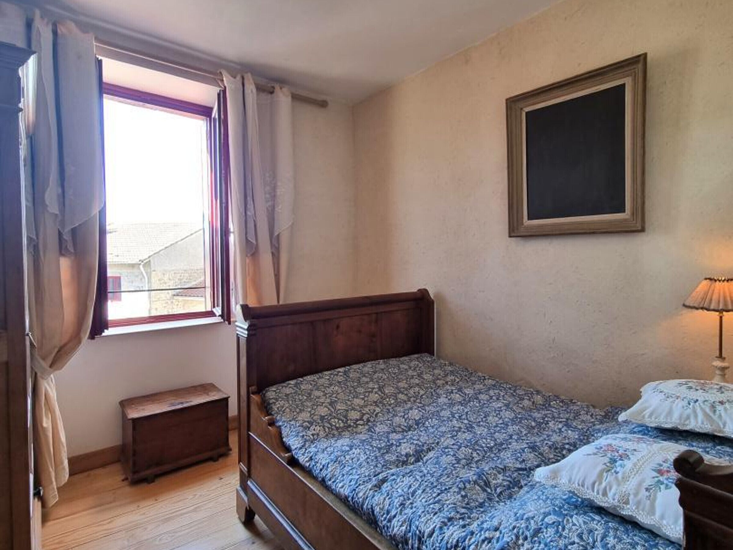 Une chambre à coucher avec un lit en bois, une petite table de chevet, une fenêtre avec des rideaux et un cadre photo fixé au mur.