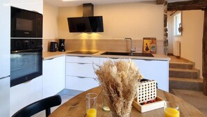 A modern kitchen with a built-in oven, microwave, and a flat-screen TV. There is a dining table with a vase of dried flowers and glasses of orange juice. - Cottage with countryside view - 2 guests (Saint-Just-Saint-Rambert)