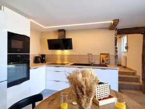 A modern kitchen with a built-in oven, microwave, and a flat-screen TV. There is a dining table with a vase of dried flowers and glasses of orange juice. - Cottage with countryside view - 2 guests (Saint-Just-Saint-Rambert)