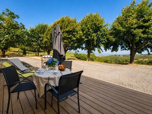 Ein Essbereich im Freien mit einem Tisch für zwei Personen, umgeben von Stühlen, einem Grill und einer Landschaftsaussicht.
