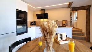 A modern kitchen with a dining table, chairs, a vase with dried flowers, and two glasses of orange juice. - Cottage with countryside view - 2 guests (Saint-Just-Saint-Rambert)