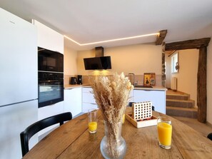 A modern kitchen with a dining table, chairs, a vase with dried flowers, and two glasses of orange juice. - Cottage with countryside view - 2 guests (Saint-Just-Saint-Rambert)