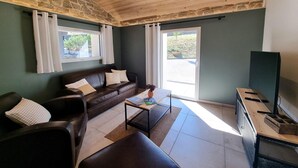 Una sala de estar con pared de piedra, techo de madera, un sofá de cuero marrón, una mesa de centro y un televisor sobre un mueble.