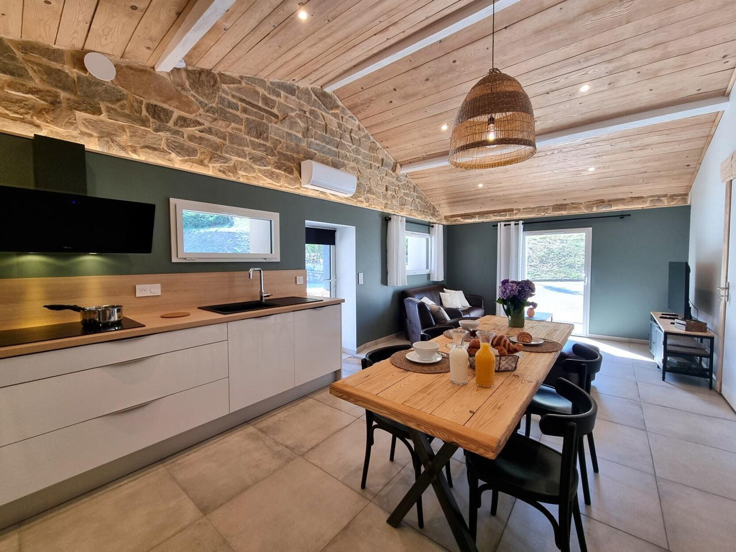 Eine moderne Küche mit einer Steinwand, Holzbalkendecke und einem Essbereich mit Tisch für zwei Personen.