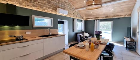 A modern kitchen with a stone wall, wooden ceiling, and a dining area with a table set for two.
