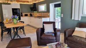 Una sala de estar moderna con sofás de cuero, un comedor con mesa de madera y una cocina con pared de piedra.