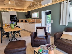 A modern living room with leather sofas, a dining area with a wooden table, and a kitchen with a stone wall. - Peaceful air-conditioned lodge - 3 guests (Saint-Just-Saint-Rambert)