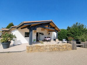 Un bâtiment à deux étages, doté de fondations en pierre, d’un patio couvert avec des sièges extérieurs et d’un petit jardin.