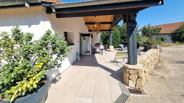 Un patio techado al aire libre con una pared de piedra, una mesa y sillas, y un letrero que dice 'Le Fayard'.