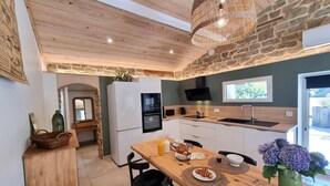 Una cocina moderna con pared de piedra, techo de madera y un comedor con mesa lista para dos.