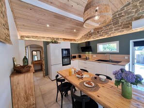 A modern kitchen with a stone wall, wooden ceiling, and a dining area with a table set for two. - Peaceful air-conditioned lodge - 3 guests (Saint-Just-Saint-Rambert)