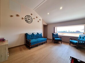 A living room with a blue sofa, a wooden chair, and a clock on the wall. - Cottage with WiFi and garden - 11 guests (SAINTE AGATHE LA BOUTERESSE)