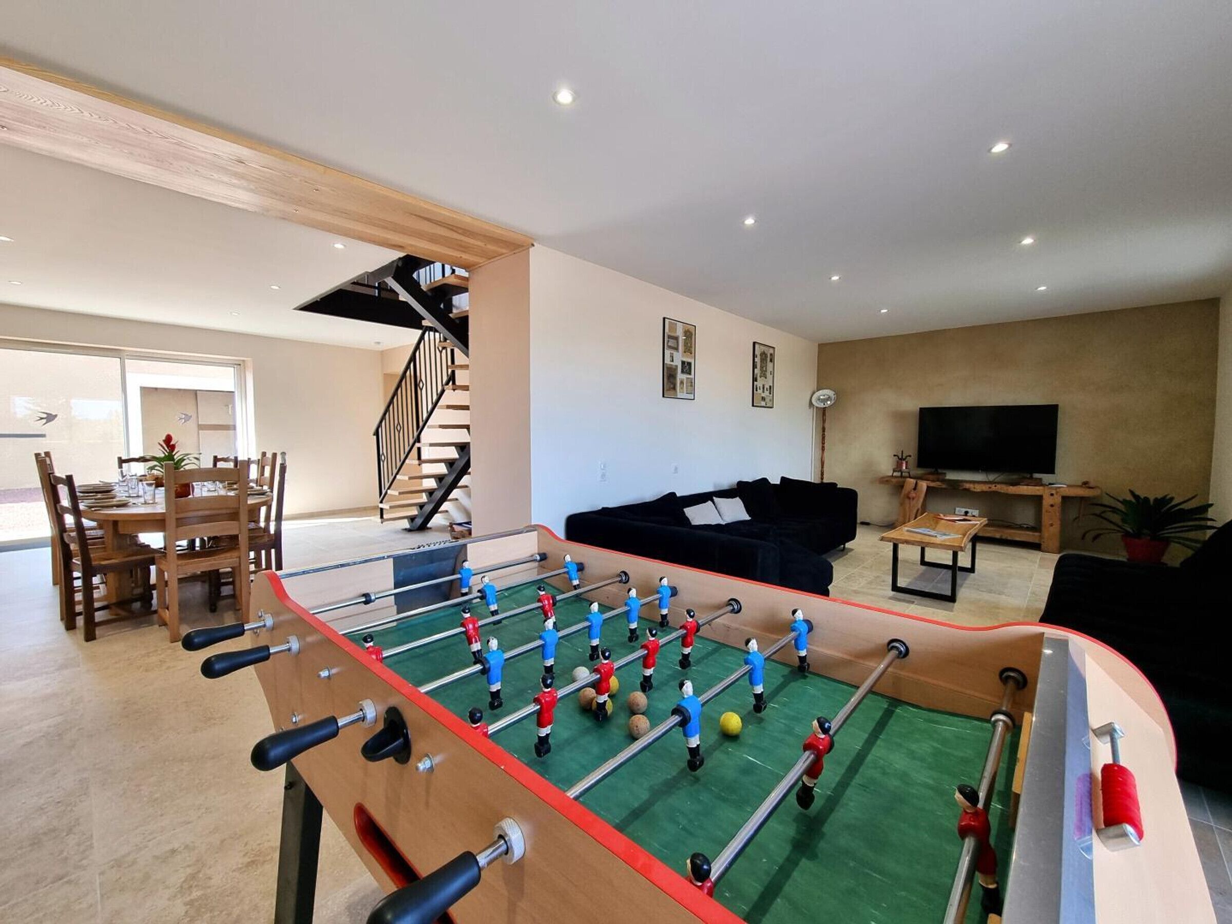 A living room with a foosball table, a sofa, a TV, and a staircase.