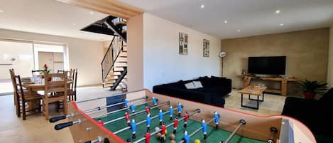 A living room with a foosball table, a sofa, a TV, and a staircase.