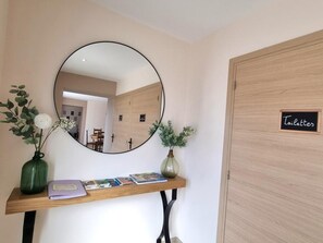 A reception area with a round mirror, a wooden console table with books, and a sign indicating the location of the toilets. - Cottage with WiFi and garden - 11 guests (SAINTE AGATHE LA BOUTERESSE)