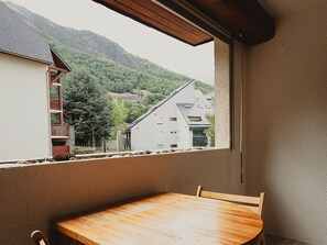 A balcony with a wooden table and chairs, overlooking a mountainous landscape with buildings. - Apartment in the heart of the village - 4 guests (Saint-Lary-Soulan)