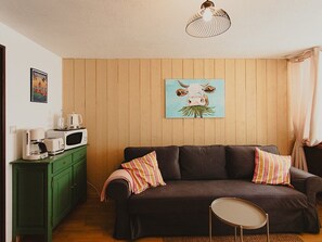 Una sala de estar acogedora con un sofá oscuro, un aparador verde, un microondas y un cuadro de una vaca.