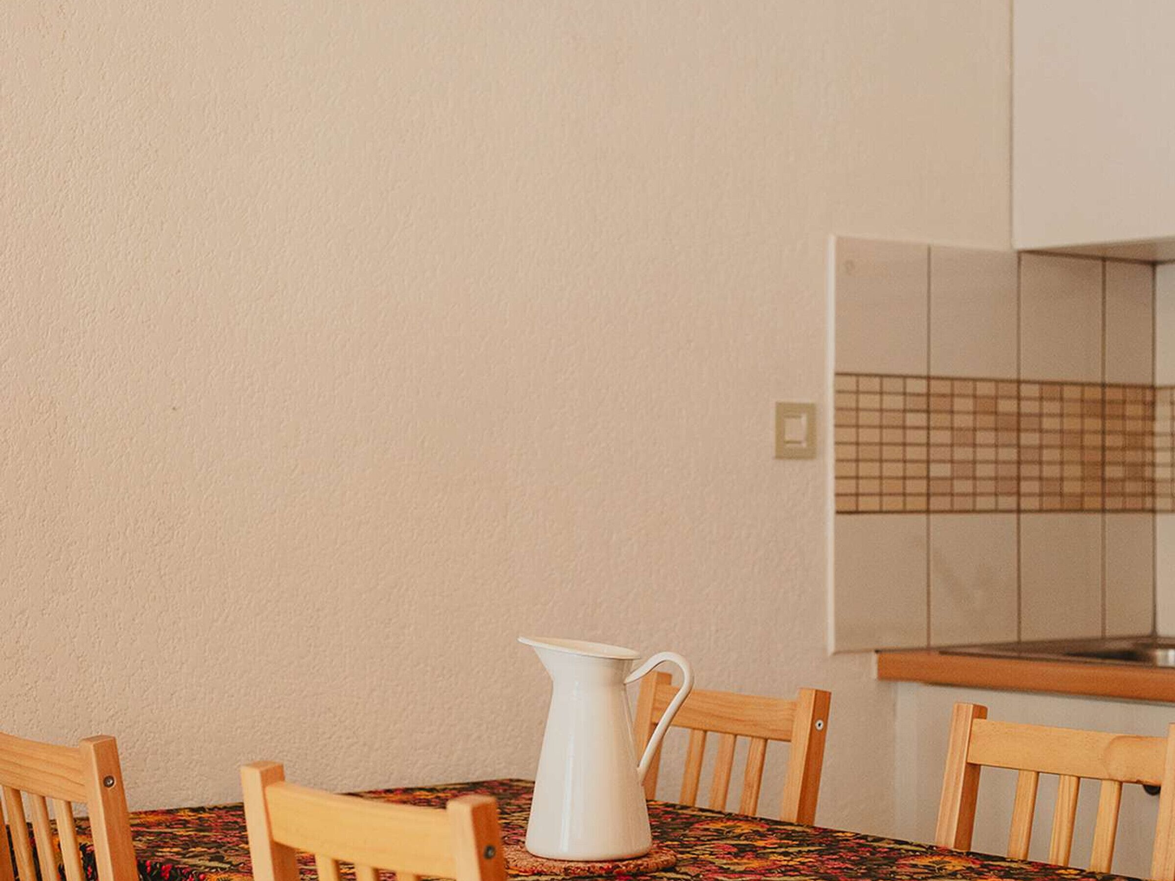 A dining table with a pitcher, wooden chairs, and a tiled backsplash in the background.