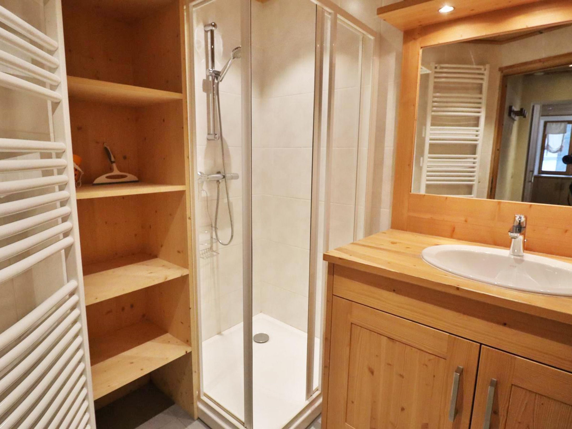 Un baño con ducha envuelta en vidrio, un tocador de madera con lavabo y un espejo sobre el tocador.