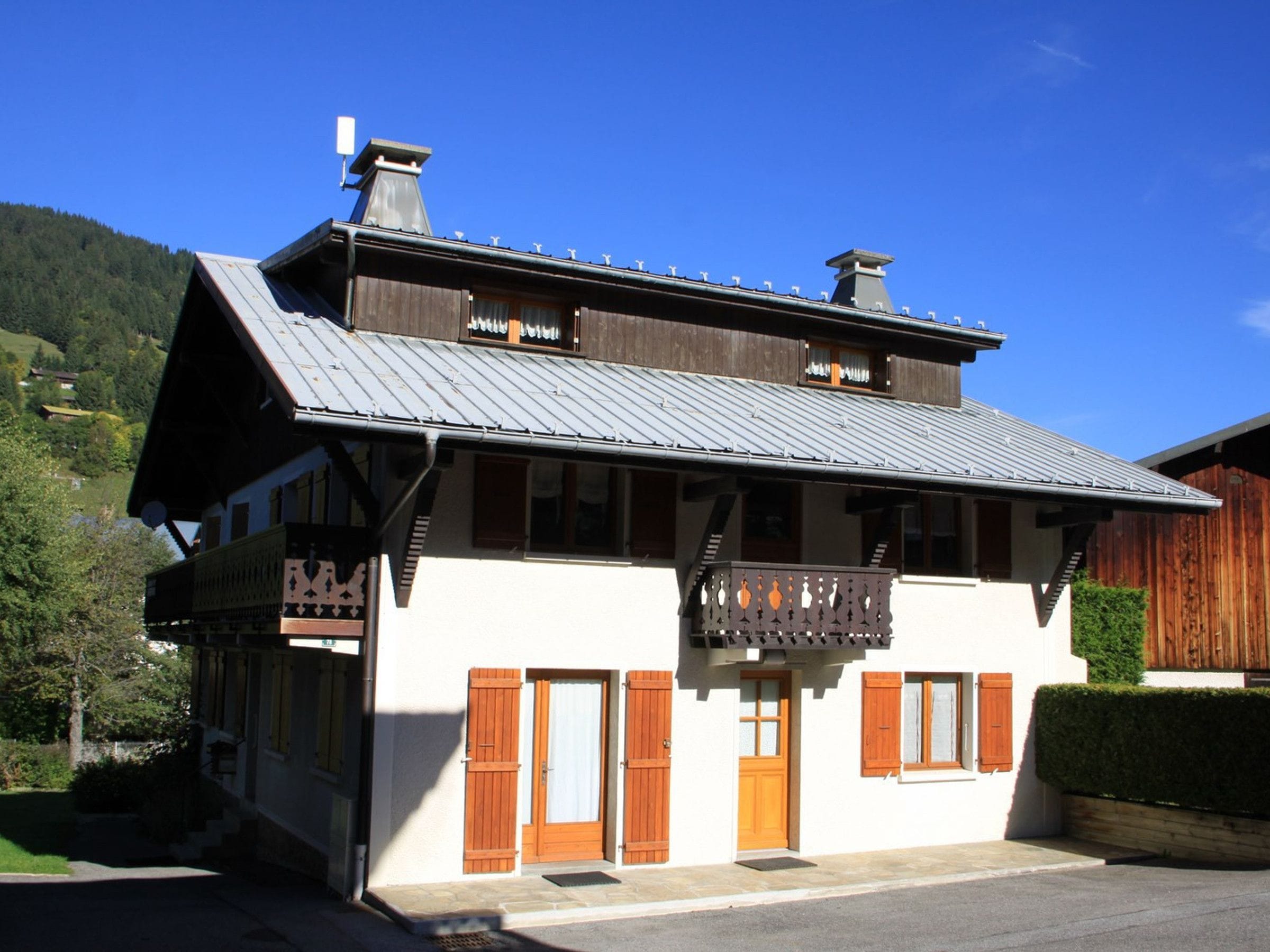 Un chalet à deux étages doté d’un balcon, de volets en bois et d’un toit en métal.