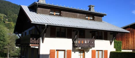 A two-story chalet with a balcony, wooden shutters, and a metal roof.