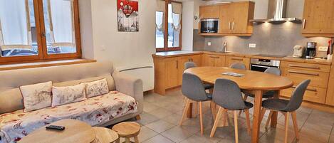 Un salon confortable avec un canapé, une petite table ronde et une table à manger avec des chaises. La cuisine est équipée d’armoires en bois et d’un four à micro-ondes.