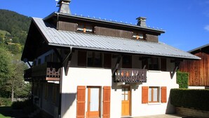 En tvåvånings chalet med en balkong, träpersienner och ett tak av metall.