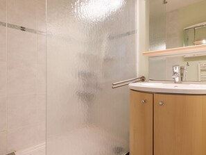 Ein Badezimmer mit Duschkabine aus Glas, einem Waschbecken mit Spiegel darüber und Holzschränken.