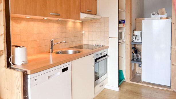 Eine kompakte Küche mit Holzausstattung, einem Edelstahl-Spülbecken, einem eingebauten Backofen und einem weißen Kühlschrank.