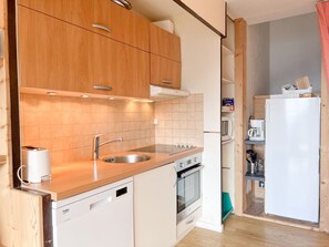 Eine kompakte Küche mit Holzausstattung, einem Edelstahl-Spülbecken, einem eingebauten Backofen und einem weißen Kühlschrank.