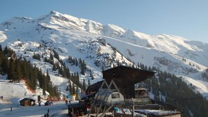 Eine Berglodge mit Seilbahn, schneebedeckten Pisten und blauem Himmel.