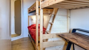 Ein Schlafraum mit Etagenbetten, einer Holzleiter, einem Schreibtisch und einer Tür.