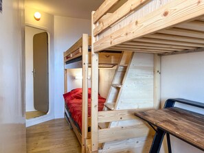 Ein Schlafraum mit Etagenbetten, einer Holzleiter, einem Schreibtisch und einer Tür.