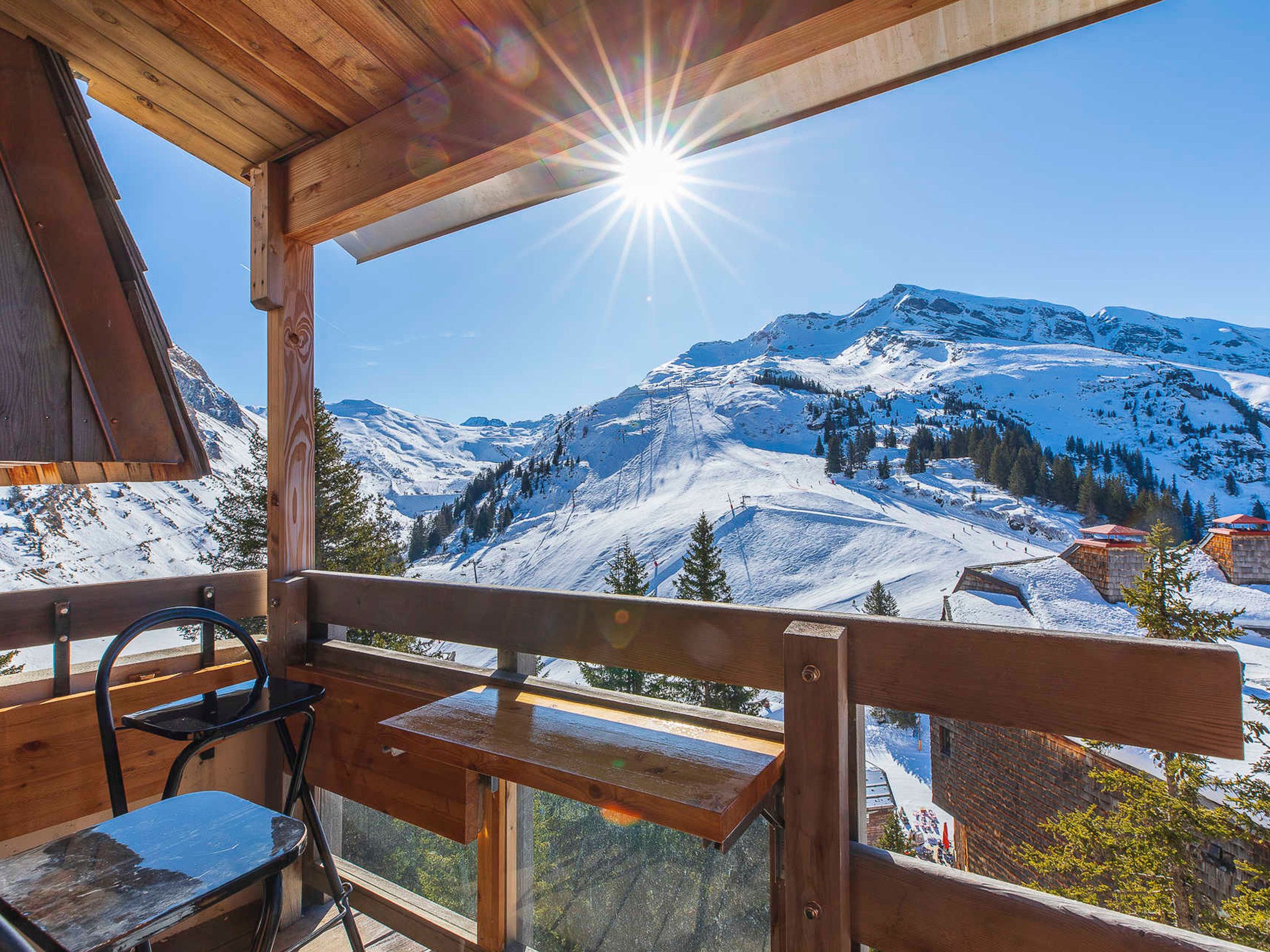 A wooden deck with a bench and a table, overlooking a snow-covered mountain landscape.