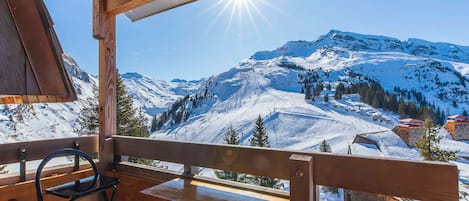 A wooden deck with a bench and a table, overlooking a snow-covered mountain landscape.