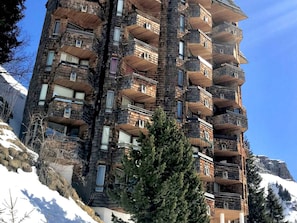 Ein mehrstöckiges Gebäude mit Balkonen, umgeben von Schnee und Bäumen.
