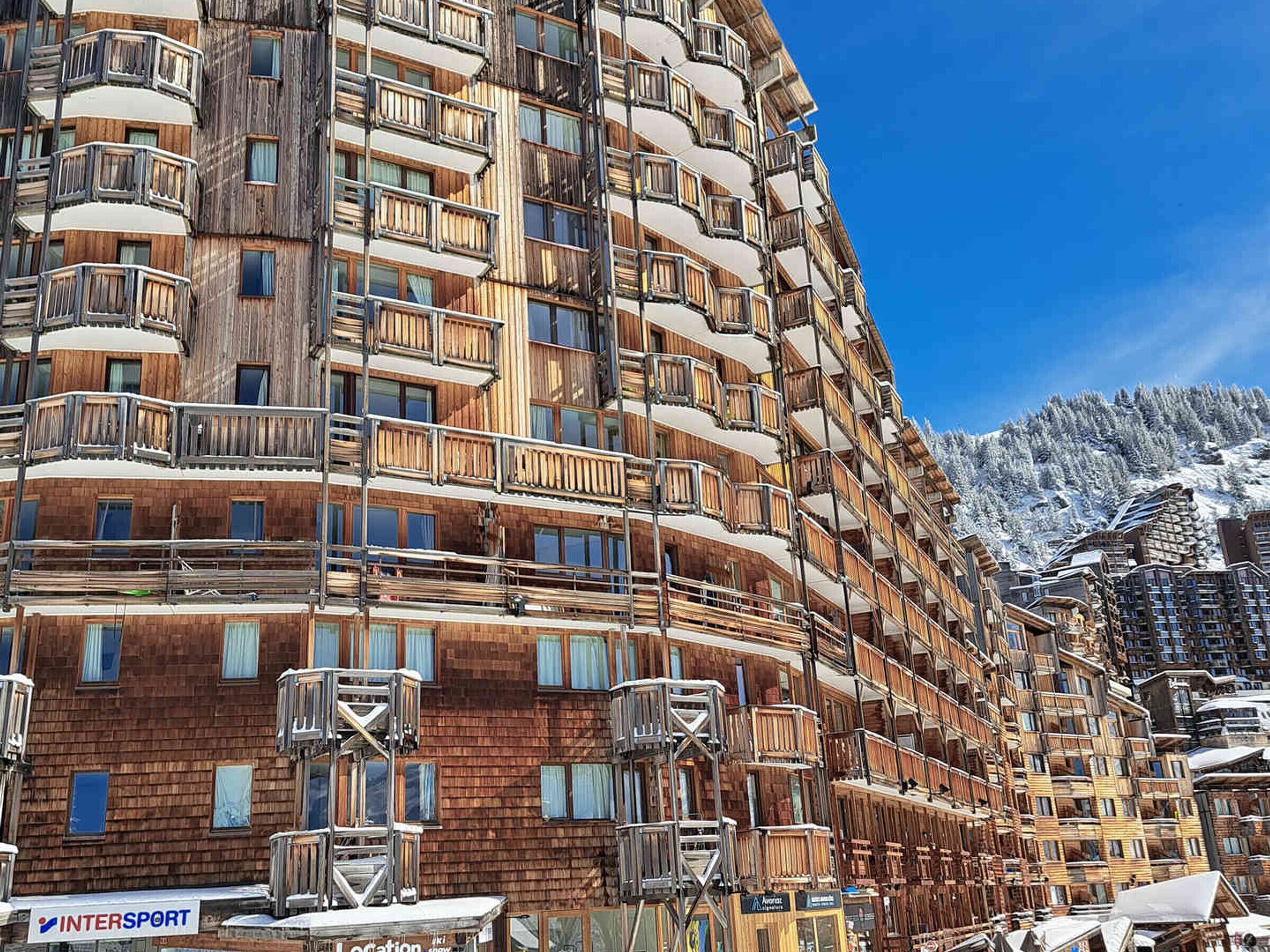 A multi-story hotel with wooden balconies and ski slope views.