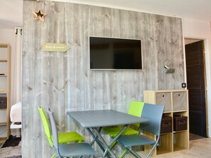 Quarto com parede de madeira, televisão de tela plana, mesa dobrável e cadeiras.