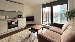 A modern kitchen with a flat-screen TV, a dining area with a sofa, and a large window with a view of the outside. - Chic 1-Bed Flat in Sheffield City Centre (Sheffield)