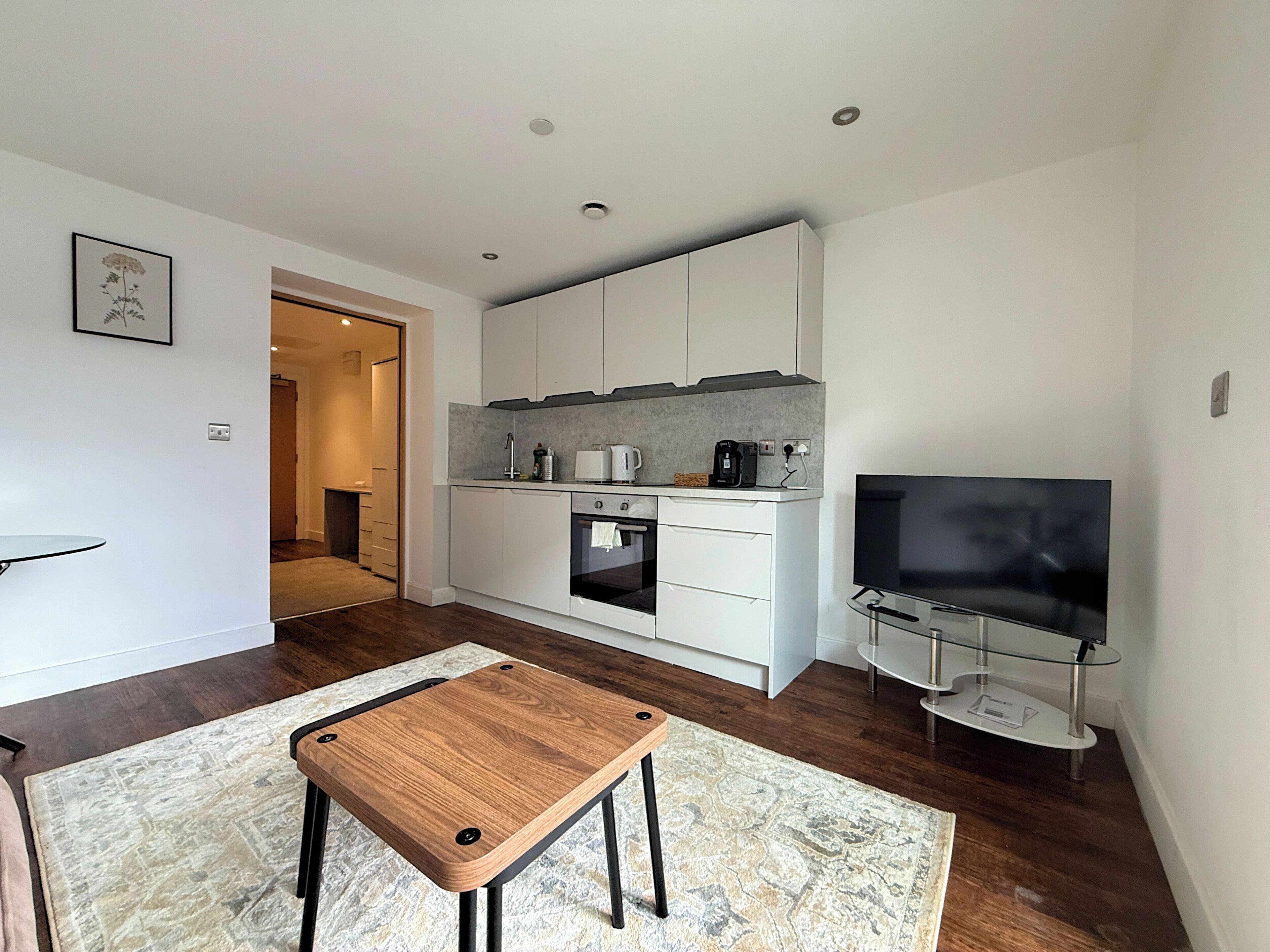A modern kitchen with white cabinets, a built-in oven, and a flat-screen TV on a glass stand.