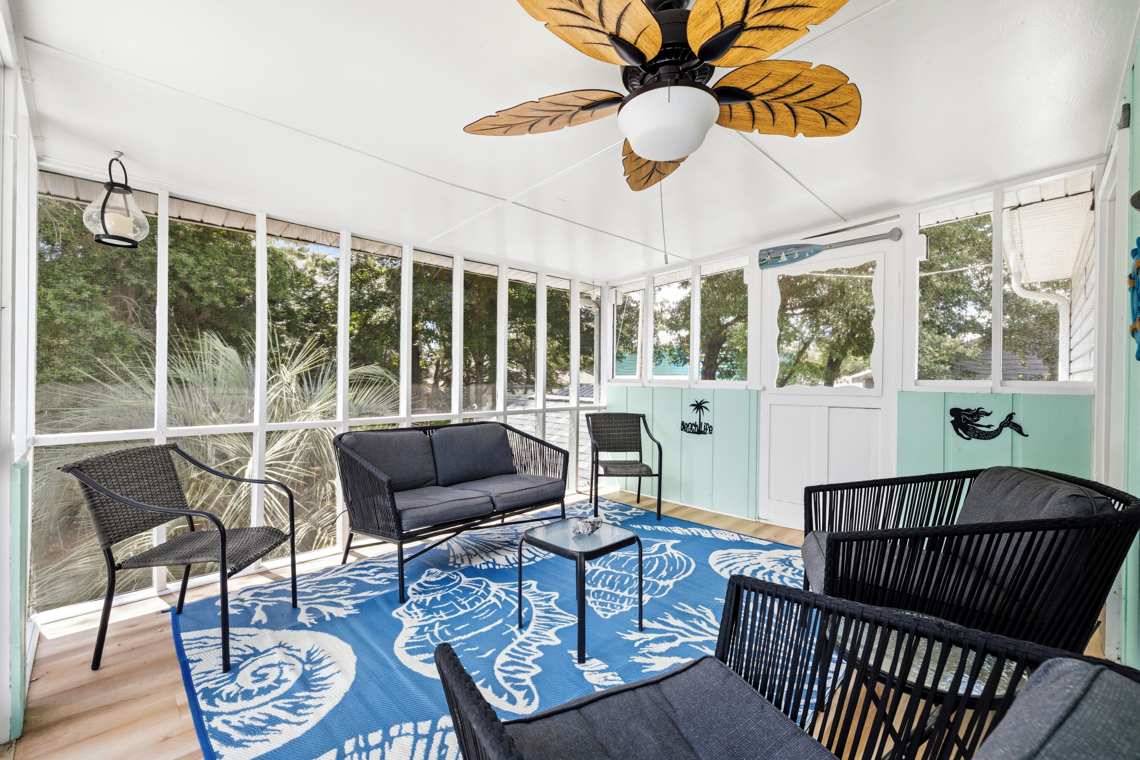A sunroom with a ceiling fan, large windows, and a blue patterned rug.