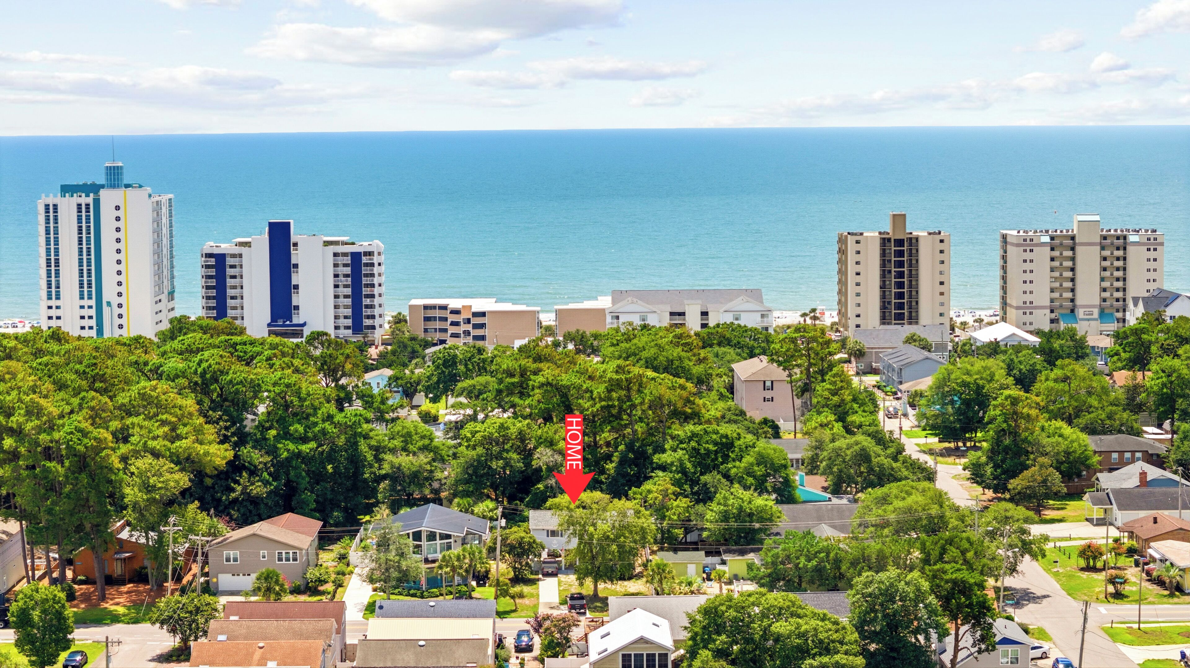 A coastal residential area with a mix of high-rise and low-rise buildings, dense greenery, and a clear view of the ocean.