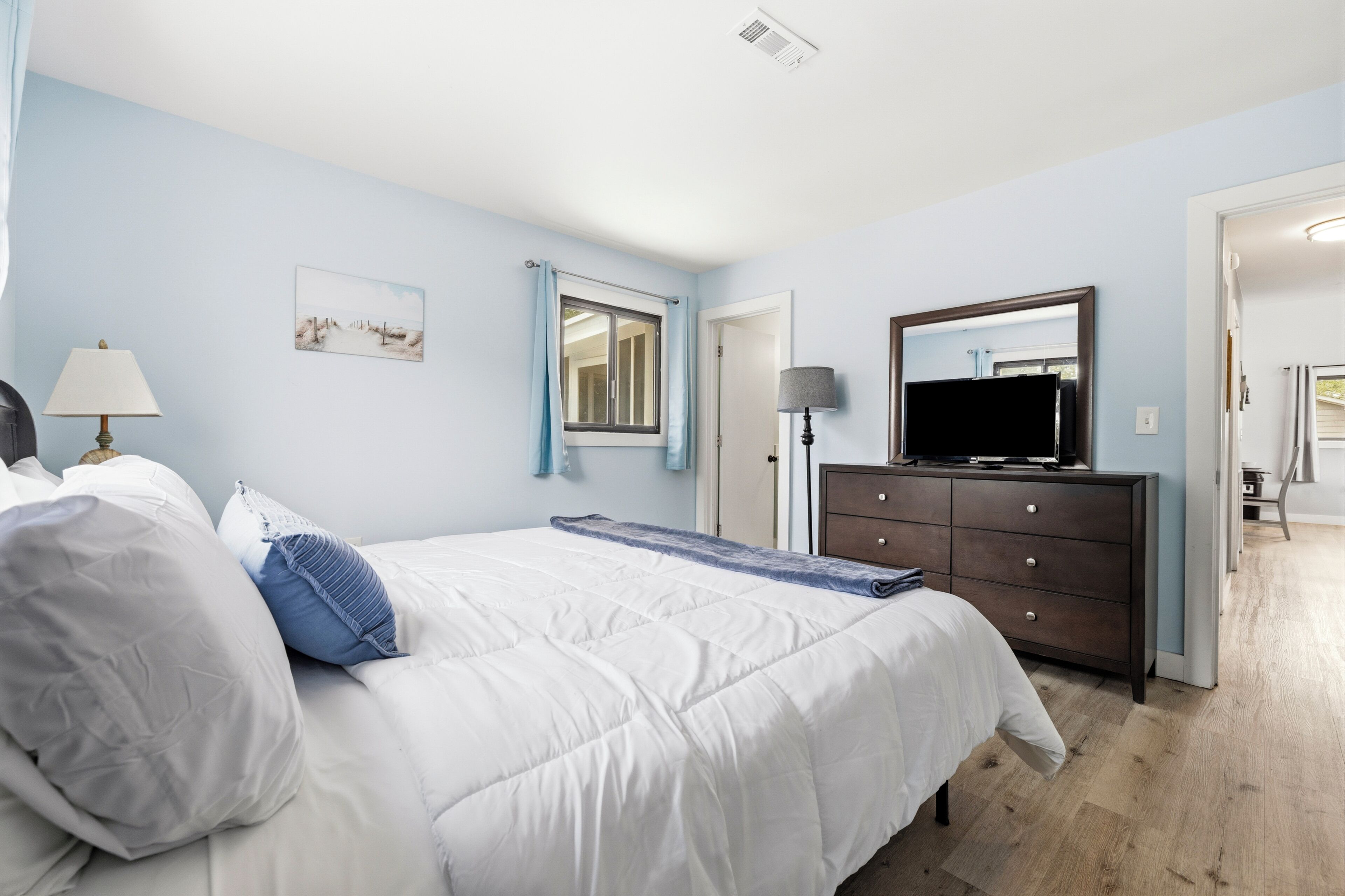 Een slaapkamer met een bed, een dressoir, een televisietoestel en een raam met gordijnen.