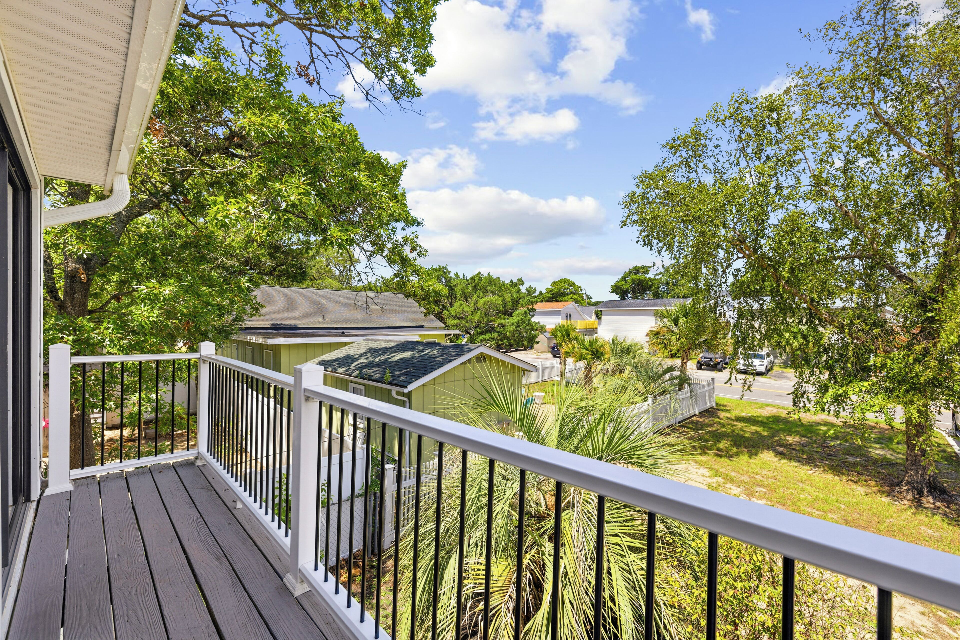 A wooden deck with a white railing overlooking a residential area with houses and trees.