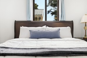 A bed with white bedding and a dark headboard, a lamp on a bedside table, and a window with a view of trees. - Walk to the Beach, North Myrtle Beach Getaway (North Myrtle Beach)
